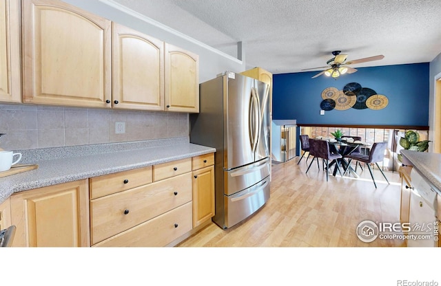 kitchen with light brown cabinetry, tasteful backsplash, a textured ceiling, stainless steel fridge, and light hardwood / wood-style floors