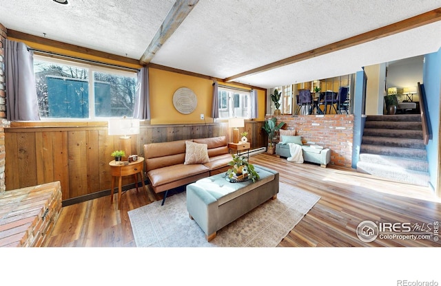 living room featuring a textured ceiling, wood-type flooring, beamed ceiling, and wood walls