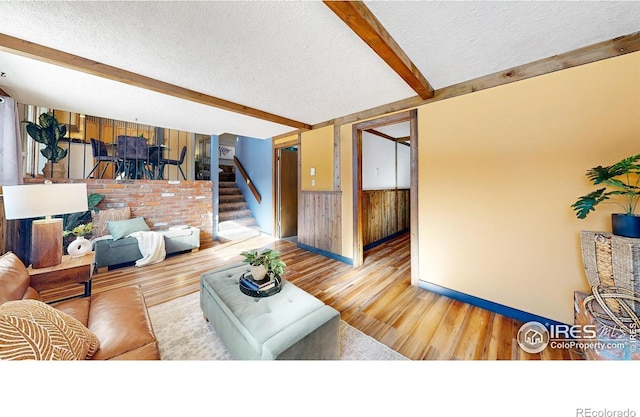 living room featuring wooden walls, hardwood / wood-style floors, beam ceiling, and a textured ceiling