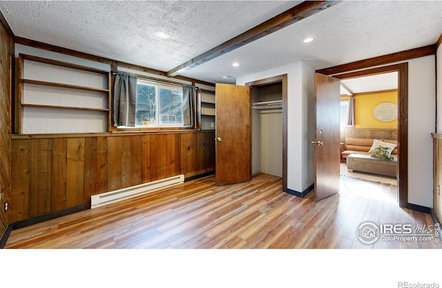 unfurnished bedroom with a closet, a textured ceiling, baseboard heating, and wood walls