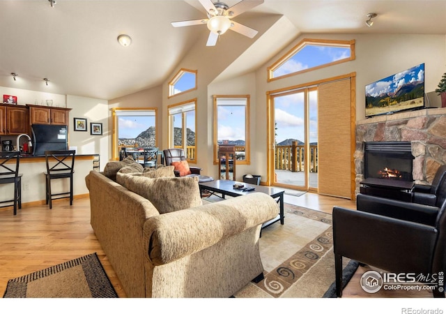 living room with a fireplace, lofted ceiling, sink, ceiling fan, and light wood-type flooring