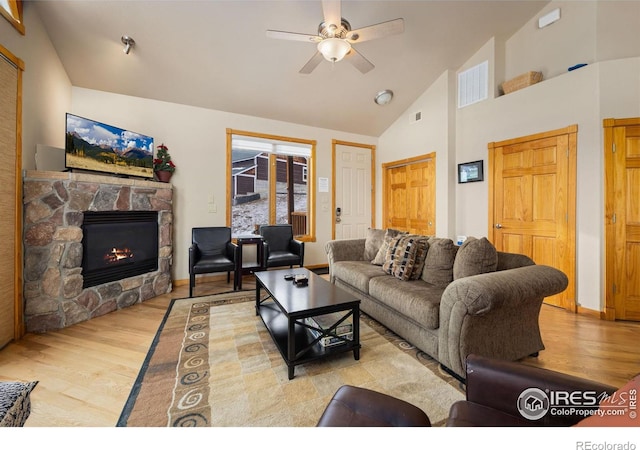 living room featuring ceiling fan, a stone fireplace, high vaulted ceiling, and light hardwood / wood-style floors