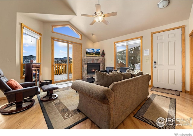 living room featuring vaulted ceiling, a stone fireplace, a healthy amount of sunlight, and light hardwood / wood-style flooring