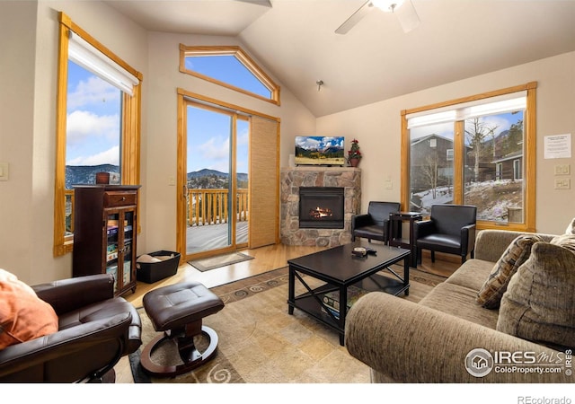 living room featuring vaulted ceiling, ceiling fan, a stone fireplace, and light hardwood / wood-style floors