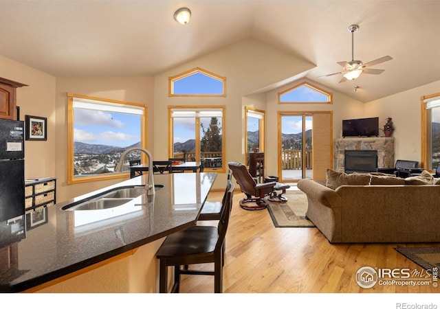 living room featuring sink, light hardwood / wood-style floors, a mountain view, a stone fireplace, and vaulted ceiling