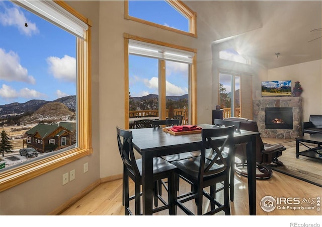 dining room featuring a mountain view, plenty of natural light, a stone fireplace, and light hardwood / wood-style flooring