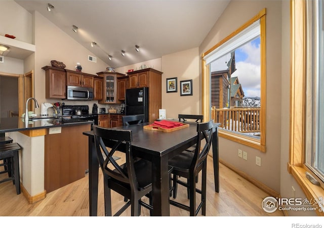 dining room featuring vaulted ceiling, sink, and light hardwood / wood-style flooring