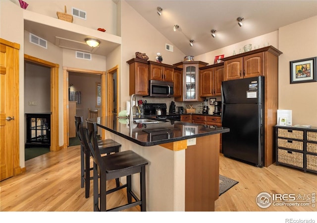 kitchen with sink, black fridge, tasteful backsplash, light hardwood / wood-style flooring, and a kitchen breakfast bar