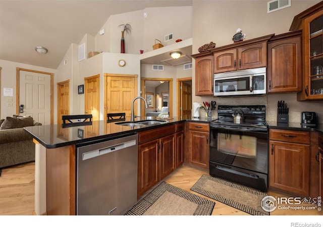 kitchen featuring sink, appliances with stainless steel finishes, high vaulted ceiling, kitchen peninsula, and light wood-type flooring