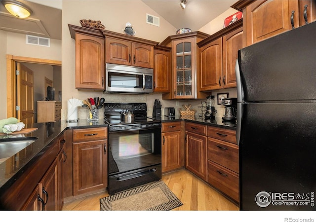 kitchen featuring light hardwood / wood-style flooring, vaulted ceiling, black appliances, and dark stone countertops