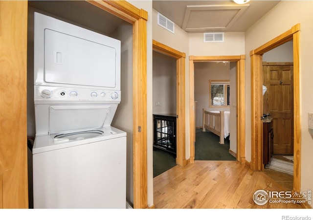 laundry room with stacked washer / drying machine and light wood-type flooring