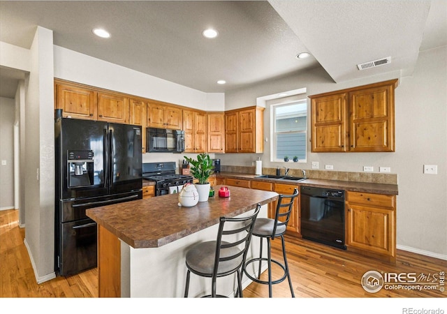 kitchen with sink, a kitchen breakfast bar, a kitchen island, light hardwood / wood-style floors, and black appliances