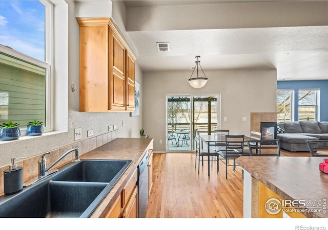 kitchen featuring sink, plenty of natural light, dishwasher, pendant lighting, and a fireplace