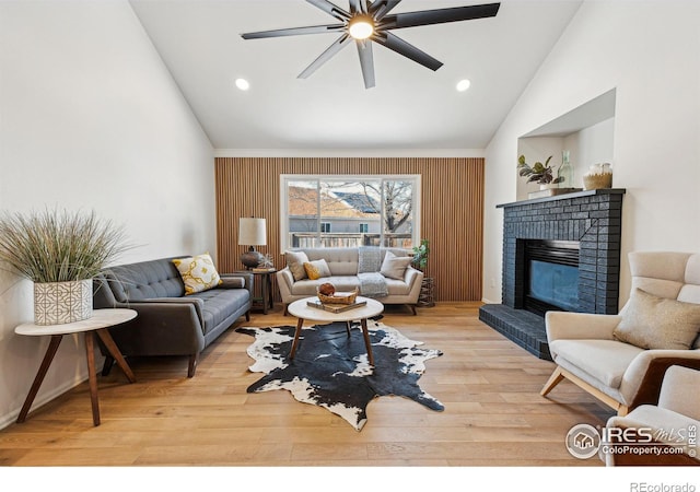 living room with vaulted ceiling, a brick fireplace, ceiling fan, and light wood-type flooring