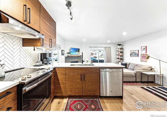 kitchen with sink, light wood-type flooring, appliances with stainless steel finishes, kitchen peninsula, and backsplash