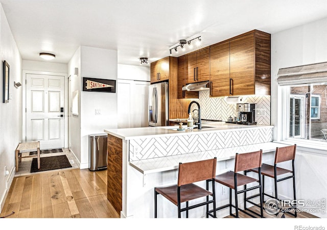 kitchen with a breakfast bar area, tasteful backsplash, light hardwood / wood-style floors, stainless steel fridge with ice dispenser, and kitchen peninsula