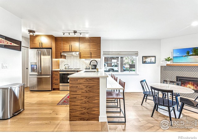 kitchen featuring sink, appliances with stainless steel finishes, a kitchen breakfast bar, light hardwood / wood-style floors, and a tiled fireplace