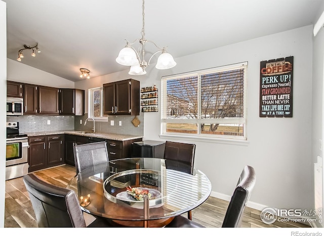 dining area featuring light hardwood / wood-style flooring, sink, vaulted ceiling, and an inviting chandelier