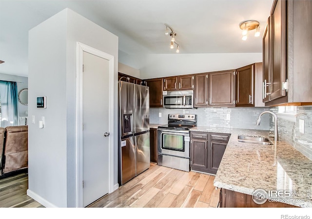 kitchen featuring sink, stainless steel appliances, light stone countertops, decorative backsplash, and light wood-type flooring