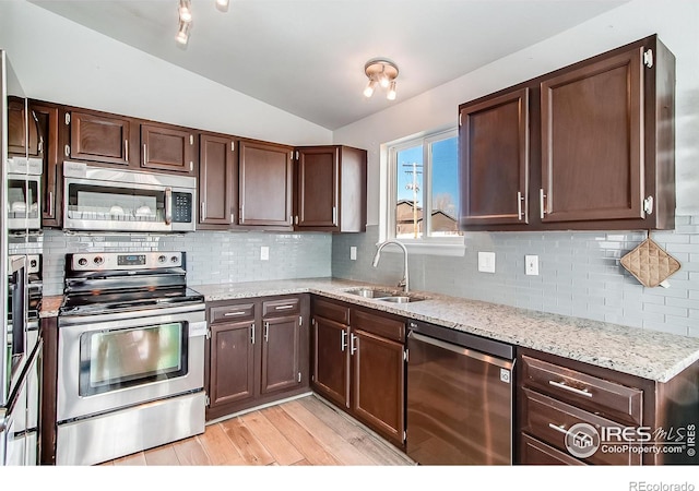 kitchen with lofted ceiling, sink, light wood-type flooring, stainless steel appliances, and decorative backsplash