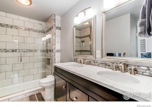 bathroom with tile patterned floors, toilet, vanity, a shower with door, and decorative backsplash