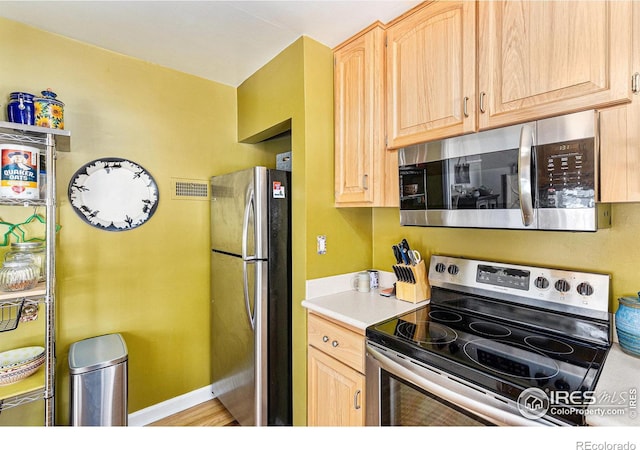 kitchen with stainless steel appliances, light brown cabinetry, and light wood-type flooring