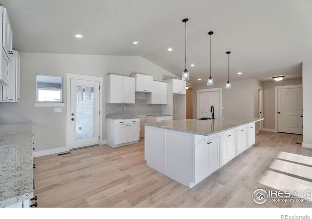 kitchen featuring sink, white cabinetry, backsplash, light stone countertops, and a center island with sink