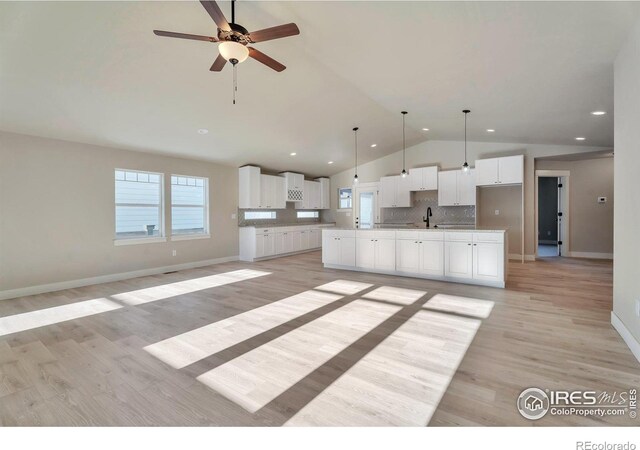 kitchen featuring pendant lighting, white cabinetry, sink, decorative backsplash, and a spacious island