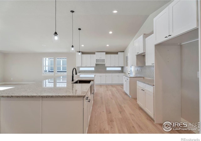 kitchen with sink, white cabinetry, hanging light fixtures, decorative backsplash, and a large island with sink