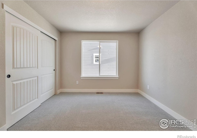 unfurnished bedroom featuring light colored carpet, a textured ceiling, and a closet