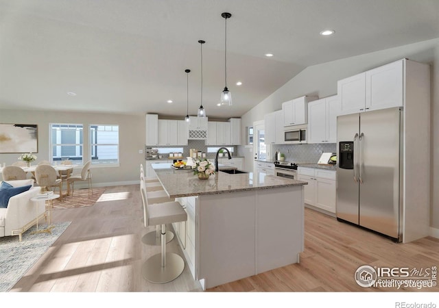 kitchen with lofted ceiling, a center island with sink, white cabinets, and appliances with stainless steel finishes