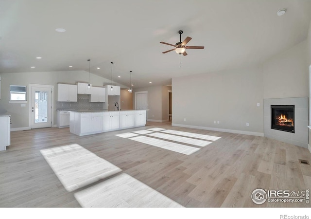 unfurnished living room with sink, vaulted ceiling, light wood-type flooring, ceiling fan, and a fireplace