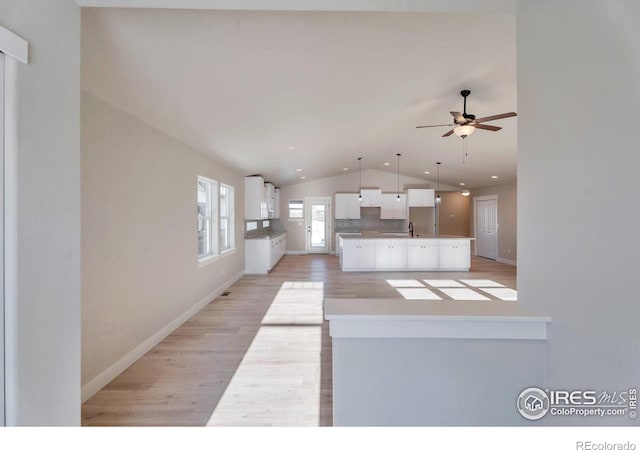 kitchen with vaulted ceiling, a kitchen island, tasteful backsplash, white cabinetry, and light hardwood / wood-style floors