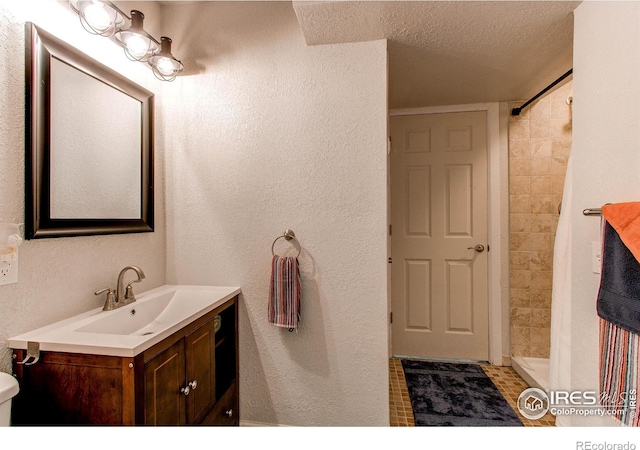 bathroom with tiled shower, vanity, and a textured ceiling