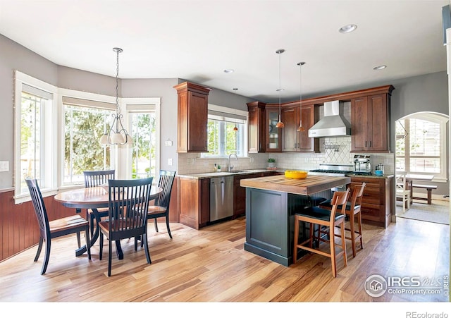 kitchen with a kitchen island, dishwasher, hanging light fixtures, wall chimney range hood, and light hardwood / wood-style flooring