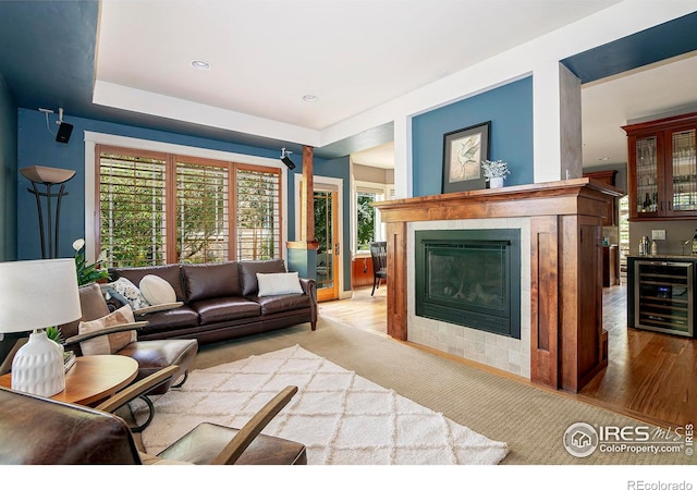 living room with a fireplace, bar area, beverage cooler, and light hardwood / wood-style floors