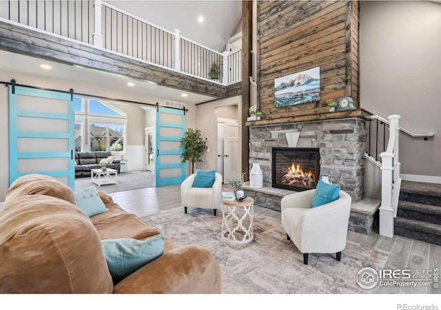 living room with a towering ceiling, a barn door, and a stone fireplace