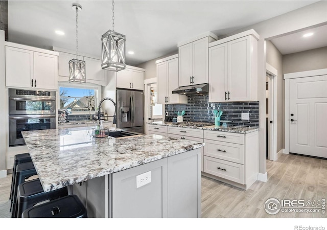 kitchen featuring a breakfast bar area, white cabinets, decorative backsplash, a large island with sink, and stainless steel appliances