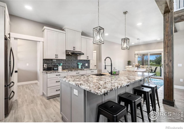 kitchen with sink, stainless steel appliances, white cabinets, a center island with sink, and decorative light fixtures