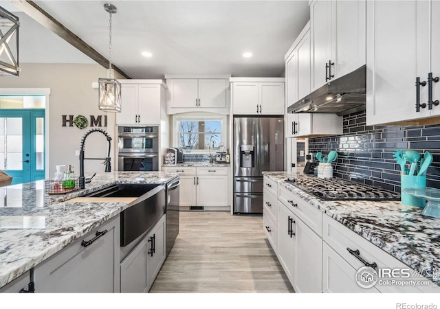 kitchen with pendant lighting, white cabinets, light stone counters, light hardwood / wood-style floors, and stainless steel appliances