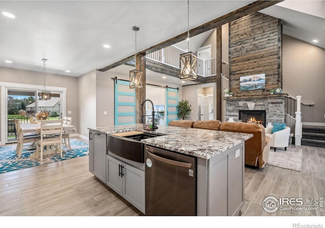 kitchen featuring light hardwood / wood-style flooring, a kitchen island with sink, stainless steel dishwasher, and decorative light fixtures