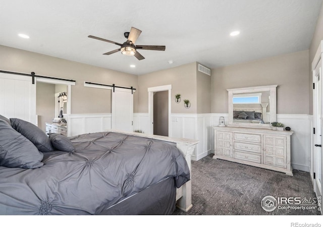 bedroom featuring a barn door, ceiling fan, and dark colored carpet