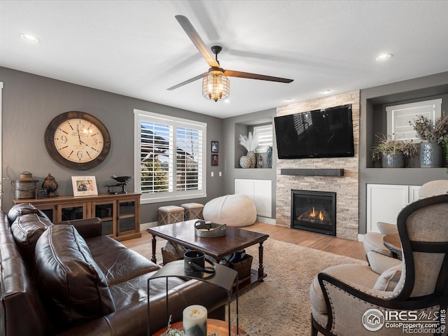 living room featuring a stone fireplace, light hardwood / wood-style floors, and ceiling fan