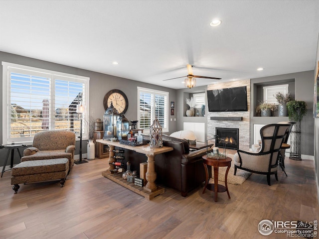 living room featuring a stone fireplace, hardwood / wood-style floors, and ceiling fan