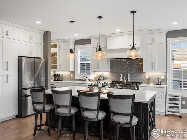 kitchen with a breakfast bar area, white cabinetry, stainless steel fridge, an island with sink, and hardwood / wood-style flooring