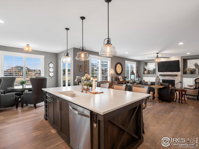 kitchen featuring stainless steel dishwasher, plenty of natural light, a kitchen island with sink, and hanging light fixtures