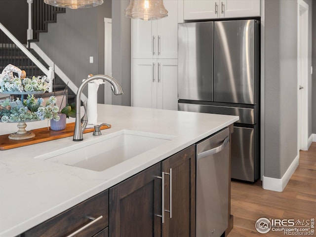 kitchen with dark brown cabinetry, sink, white cabinetry, wood-type flooring, and stainless steel appliances