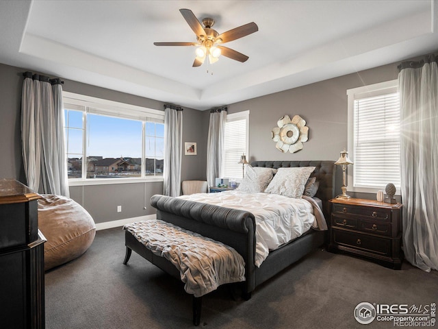 bedroom featuring ceiling fan, a raised ceiling, and dark colored carpet