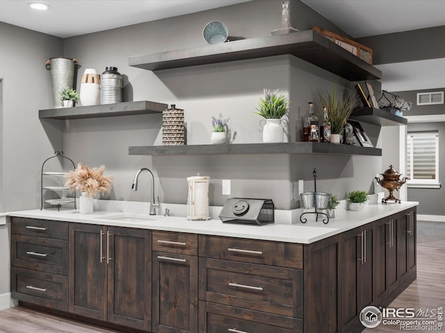 bar featuring sink, dark brown cabinetry, and light hardwood / wood-style floors