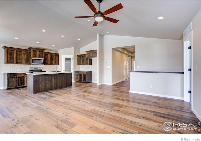 kitchen featuring vaulted ceiling, a center island with sink, light wood-type flooring, appliances with stainless steel finishes, and decorative backsplash